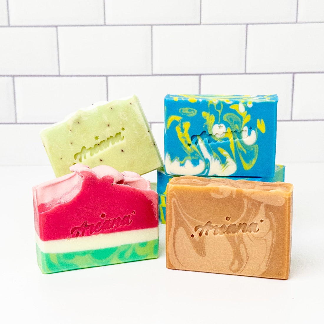 Four colorful soap bars on a white background with a tiled wall.