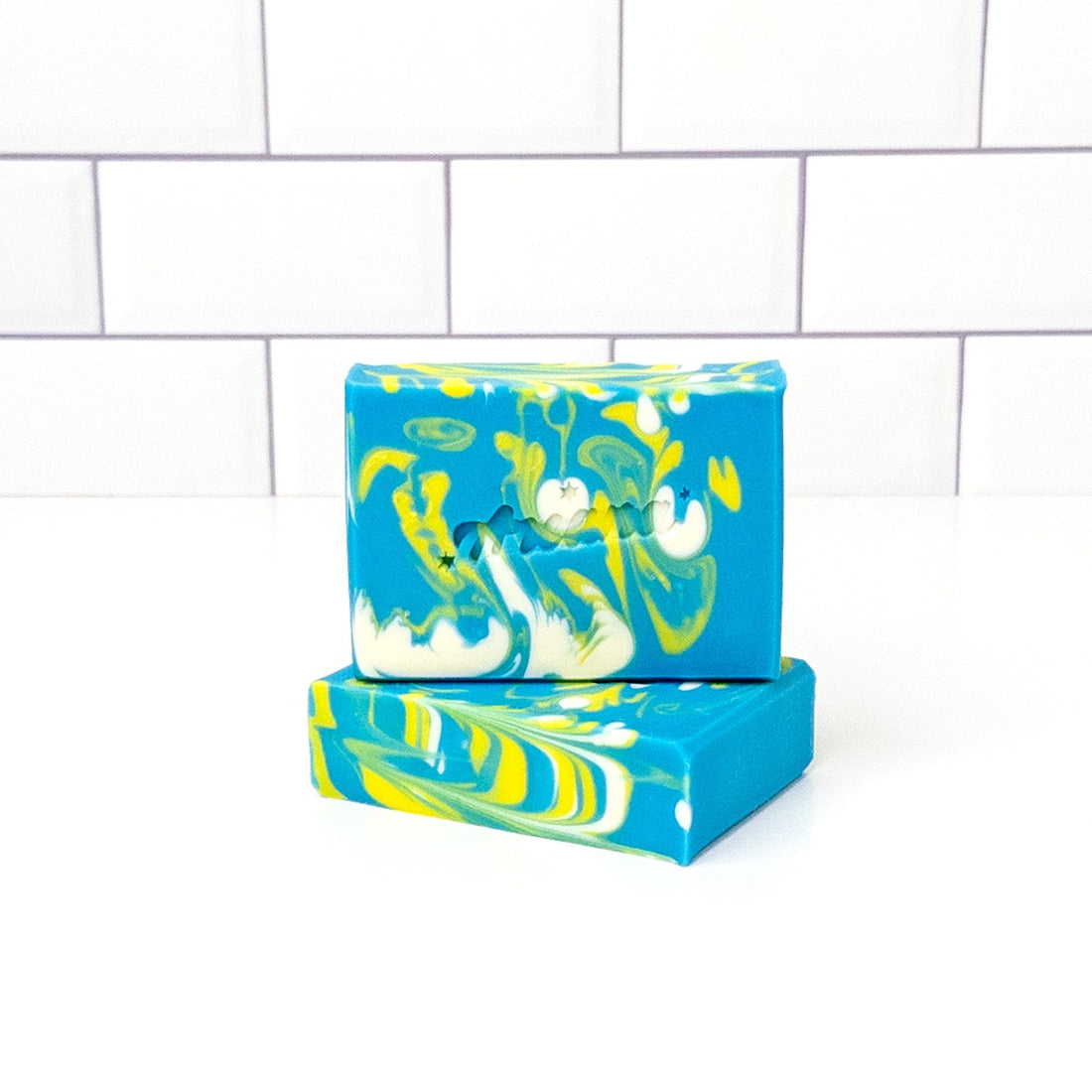 Two blue and green marbled soap bars on a white tiled background